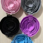 Set de 5 moldes de silicona apilables para freidora de aire en colores rosa, gris, negro, morado y azul, con diseño acanalado y asas laterales.
