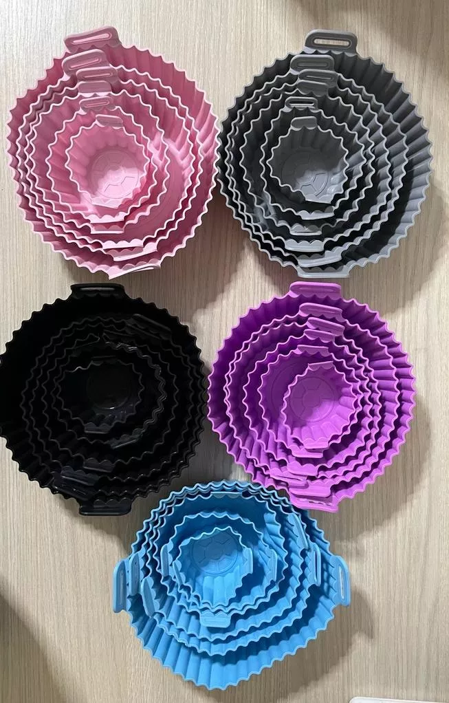 Set de 5 moldes de silicona apilables para freidora de aire en colores rosa, gris, negro, morado y azul, con diseño acanalado y asas laterales.