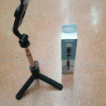 Trípode para celular con luz LED integrado, color negro, en caja azul.
