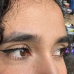 Primer plano de ojos con delineado cat eye, pestañas y cejas pobladas, cabello rizado oscuro.