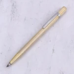 Bolígrafo dorado con textura diamantada y clip metálico plateado, sobre fondo claro texturizado.