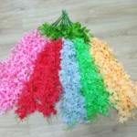 Set de 6 glicinias artificiales colgantes en colores vibrantes: rosa, rojo, azul, verde, melocotón y amarillo sobre suelo de madera.