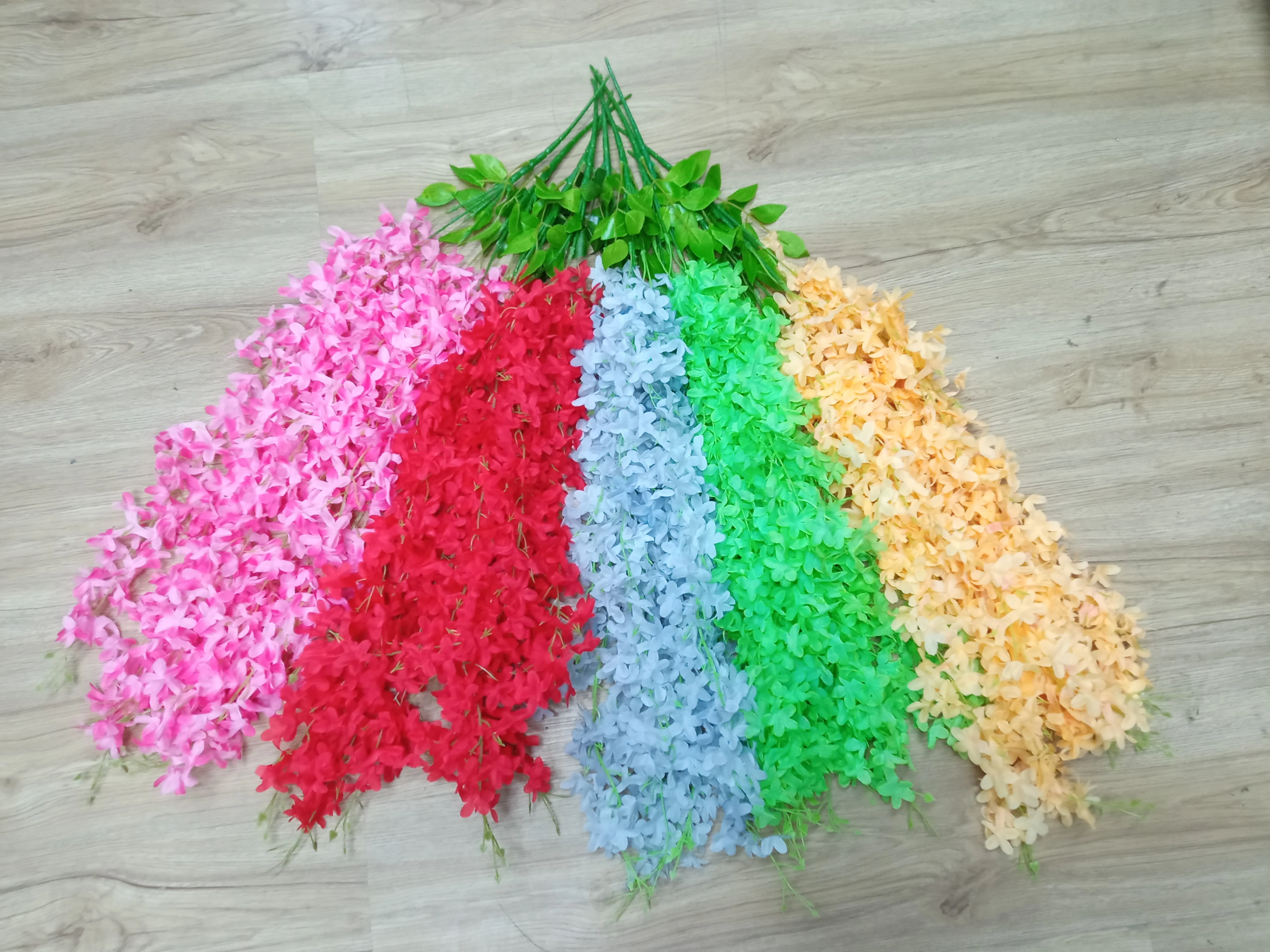 Set de 6 glicinias artificiales colgantes en colores vibrantes: rosa, rojo, azul, verde, melocotón y amarillo sobre suelo de madera.