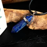 Colgante de lapislázuli facetado azul con inclusiones doradas, montado en aro plateado y cordón negro.