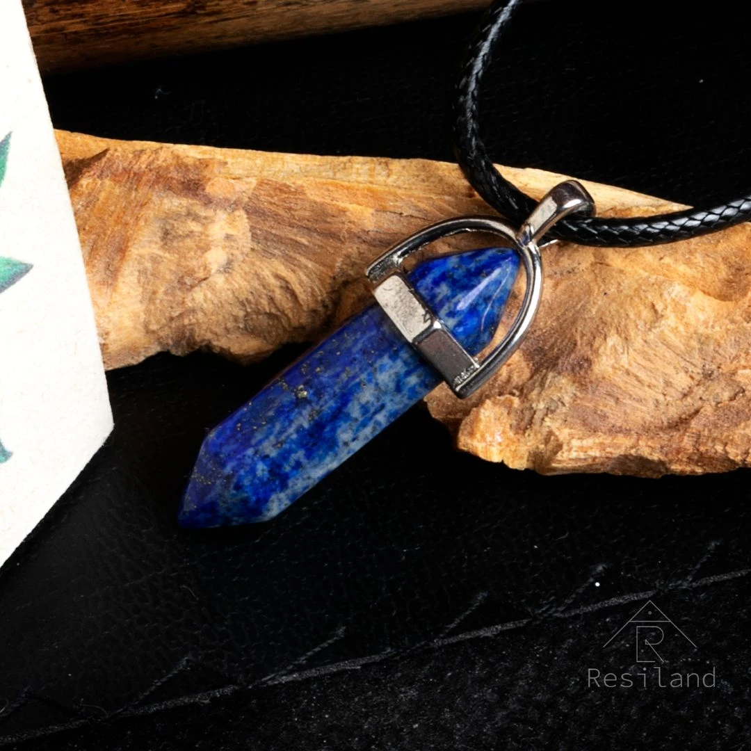 Colgante de lapislázuli facetado azul con inclusiones doradas, montado en aro plateado y cordón negro.