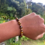 Pulsera de ojo de tigre y cuentas doradas en muñeca con fondo natural, accesorio para potenciar la confianza.