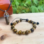 Set pulsera y colgante ojo de tigre con cuentas doradas sobre madera, ideal para potenciar confianza y concentración.