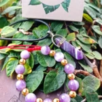 Kit de amatista: colgante con dije puntiforme y pulsera de cuentas violetas y doradas, sobre follaje verde.