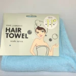 Toalla azul de microfibra para secado rápido de cabello en su empaque original de cartón, que incluye instructivo con pasos para su uso.