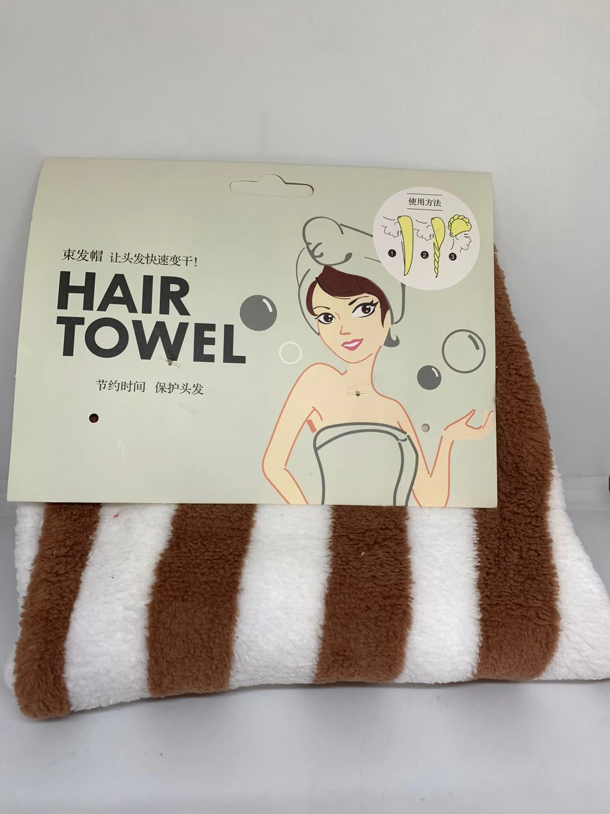 Toalla de microfibra para secar el cabello con estampado de rayas café y blancas, empacada con cartón informativo que ilustra paso a paso su uso.
