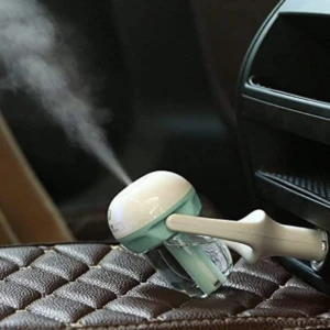 Humidificador ambientador para carro, blanco y verde, emitiendo vapor sobre asiento de cuero.