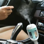 Humidificador ambientador para carro, blanco y azul, atomizando vapor dentro de un vehículo.