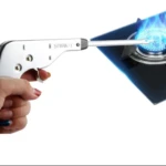 Pistola encendedor de gas plateada en mano, encendiendo quemador de estufa vitrocerámica azul.