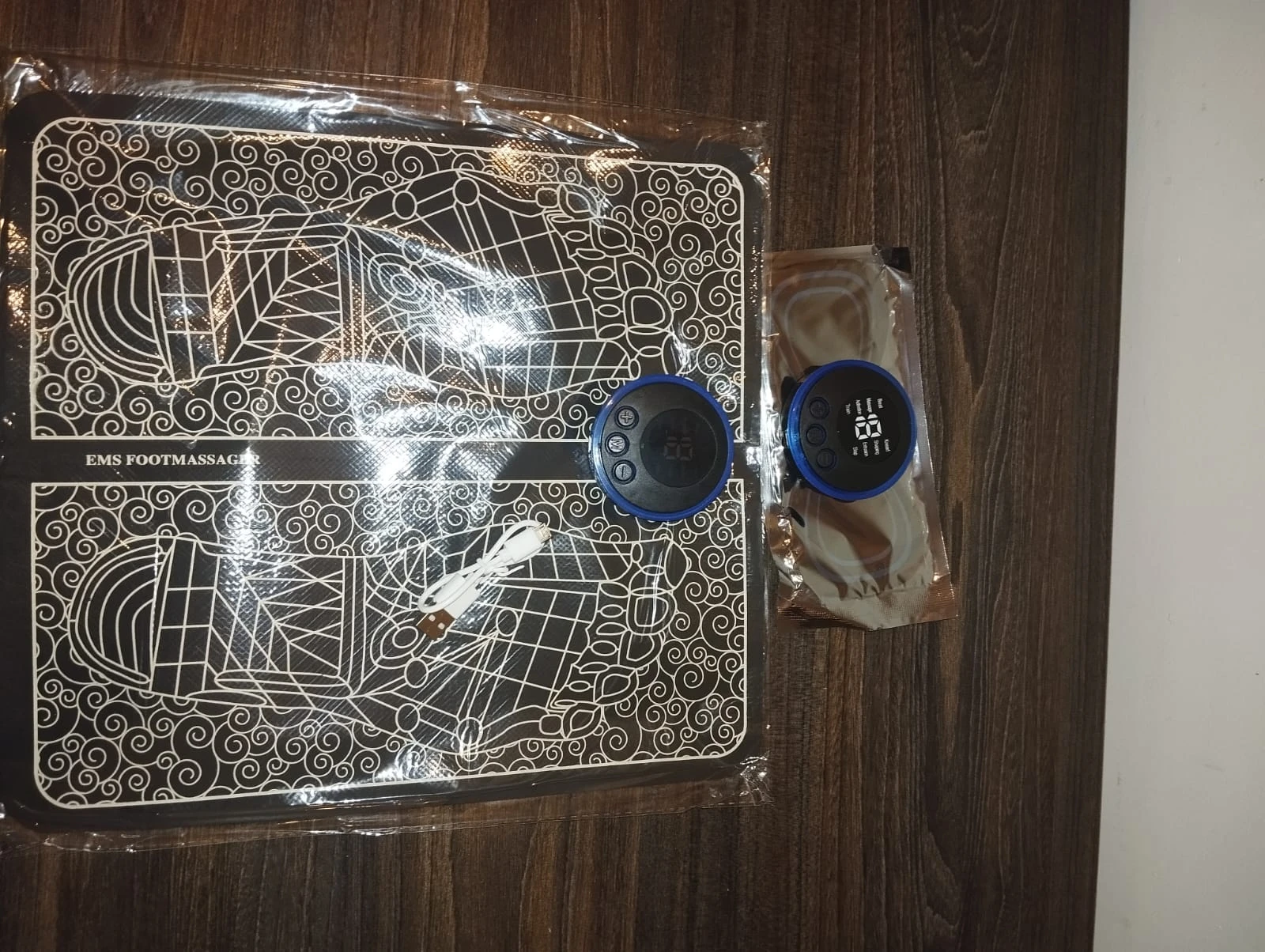 Tapete masajeador EMS de pies con diseño estampado, dos controles circulares azules y cable USB.