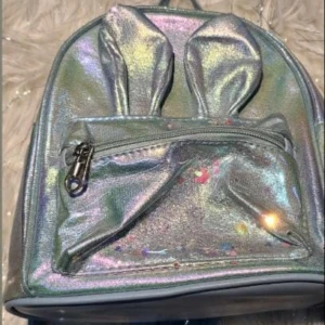 Bolso metálico holográfico infantil con orejas de conejo, bolsillo frontal con cierre.