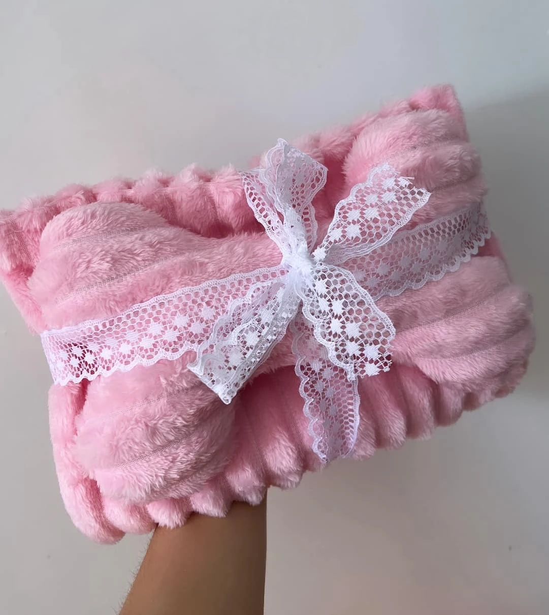 Kit cobija y almohada doble faz rosa, suave, con encaje blanco y moño, sostenido en mano.