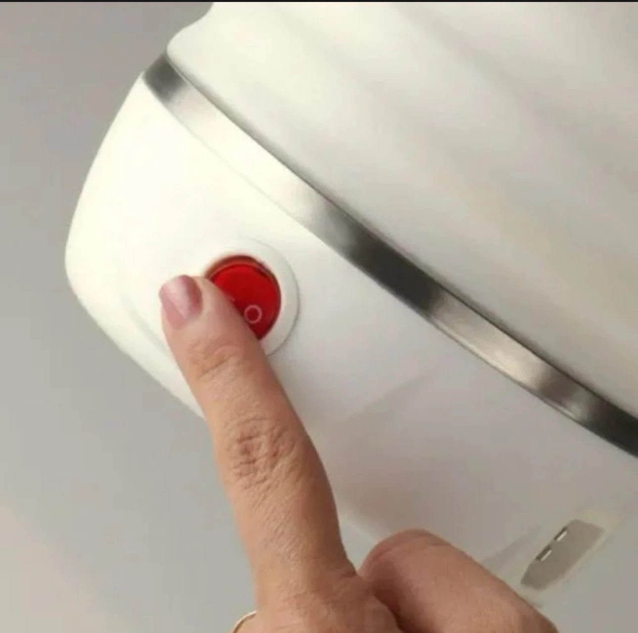 Primer plano de una jarra eléctrica de silicona blanca con base metálica, donde un dedo presiona el interruptor de encendido rojo en el costado.