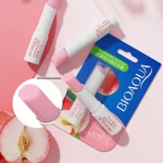 Dos bálsamos labiales reparadores Bioaqua con tapa rosa, uno abierto, sobre fondo con duraznos.