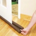 Tapon aislante de puerta doble marrón de espuma, colocado en suelo de madera.