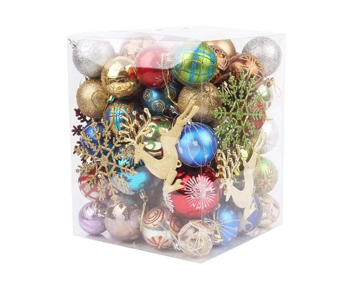 Caja cúbica transparente con surtido de bolas navideñas colgantes plásticas decorativas en colores rojo, azul, dorado, plateado y verde, adornadas con renos dorados y copos de nieve.