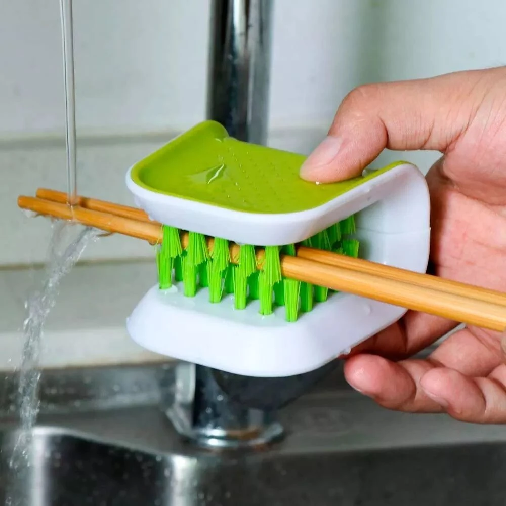 Cepillo verde y blanco para limpiar palillos bajo el grifo, diseño compacto y funcional para cocina.