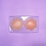 Par de cubrepezones invisibles de silicona color piel, con diseño en forma de flor, empacados en blíster plástico transparente sobre fondo morado.