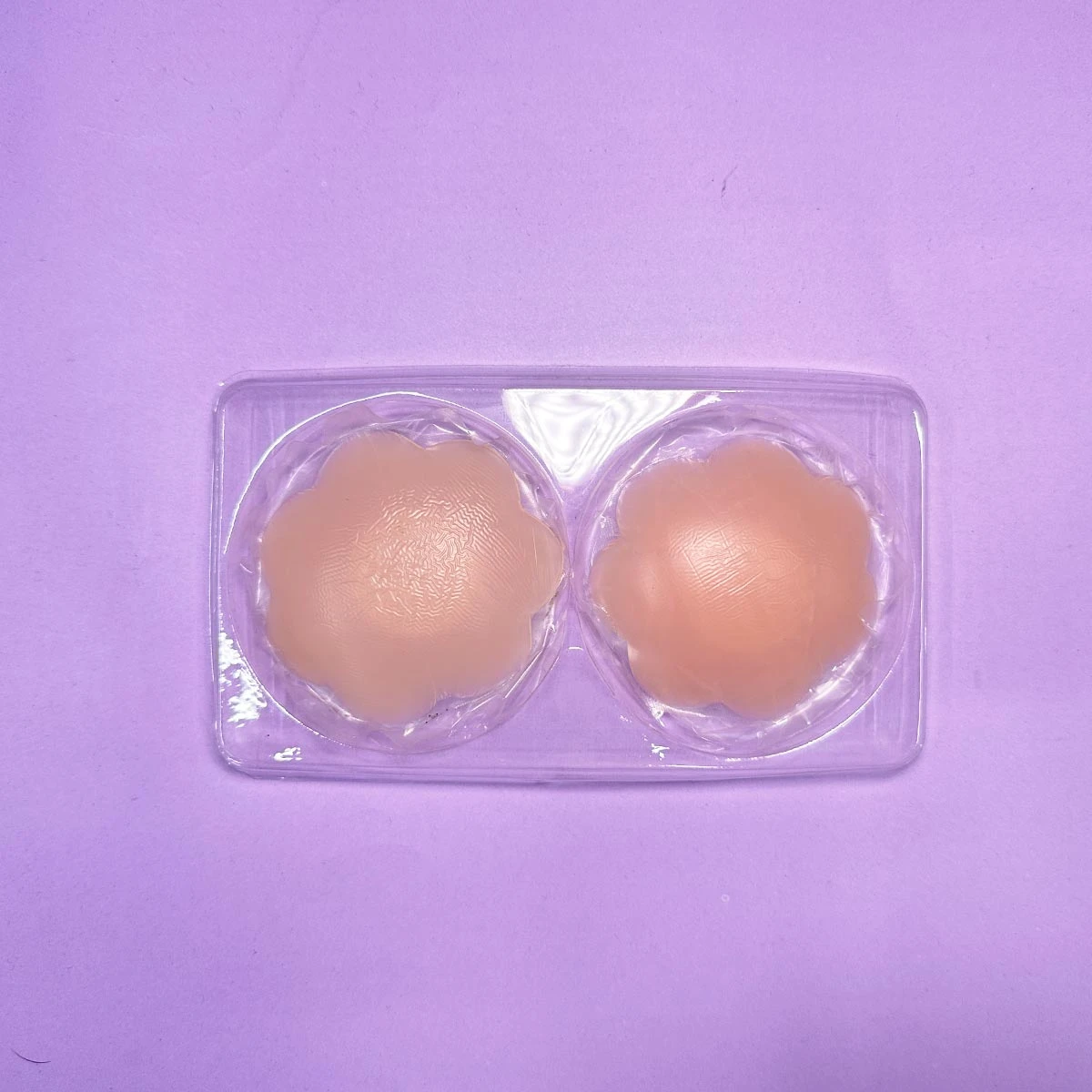 Par de cubrepezones invisibles de silicona color piel, con diseño en forma de flor, empacados en blíster plástico transparente sobre fondo morado.
