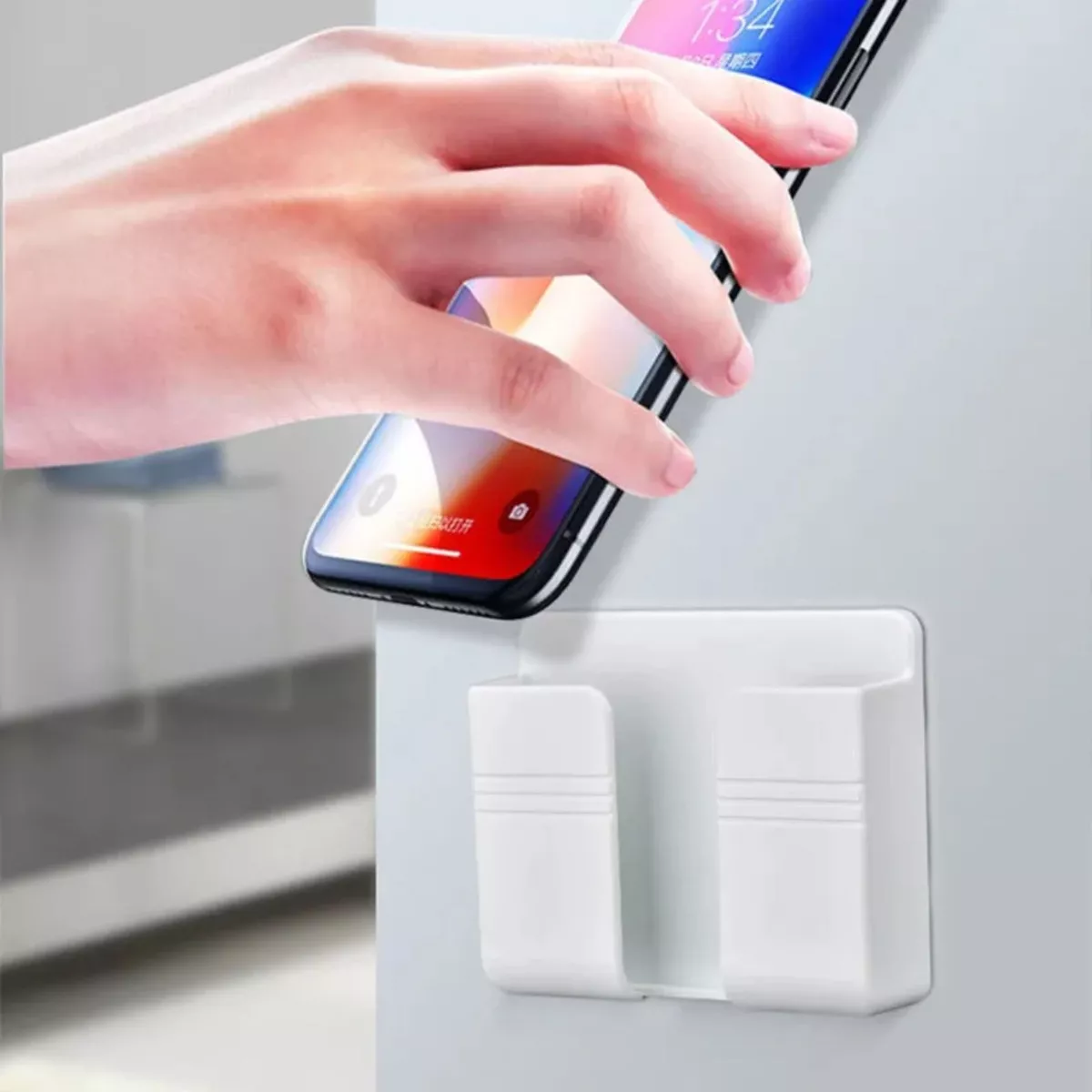 Soporte blanco para celular adherido a la pared, con mano colocando un iPhone.
