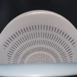 Colador blanco de plástico con perforaciones lineales y circulares.