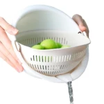 Colador escurridor blanco giratorio con verduras verdes, agua fluyendo por el lateral.