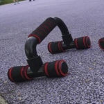 Soportes negros para push-up con agarres acolchados rojos, ideales para entrenamientos en exteriores.