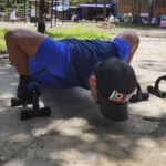 Soporte para push up negro con agarraderas para entrenamiento, usado por hombre en suelo de cemento.