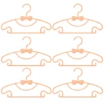 Seis ganchos para ropa de bebé color salmón con forma de moño, ideales para colgar y organizar prendas.