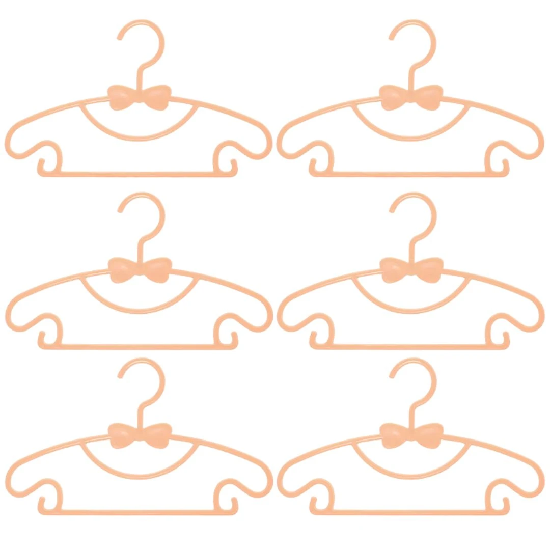 Seis ganchos para ropa de bebé color salmón con forma de moño, ideales para colgar y organizar prendas.