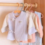 Ganchos flexibles para ropa de bebé en tonos pastel, organizados en un tendedero de madera.