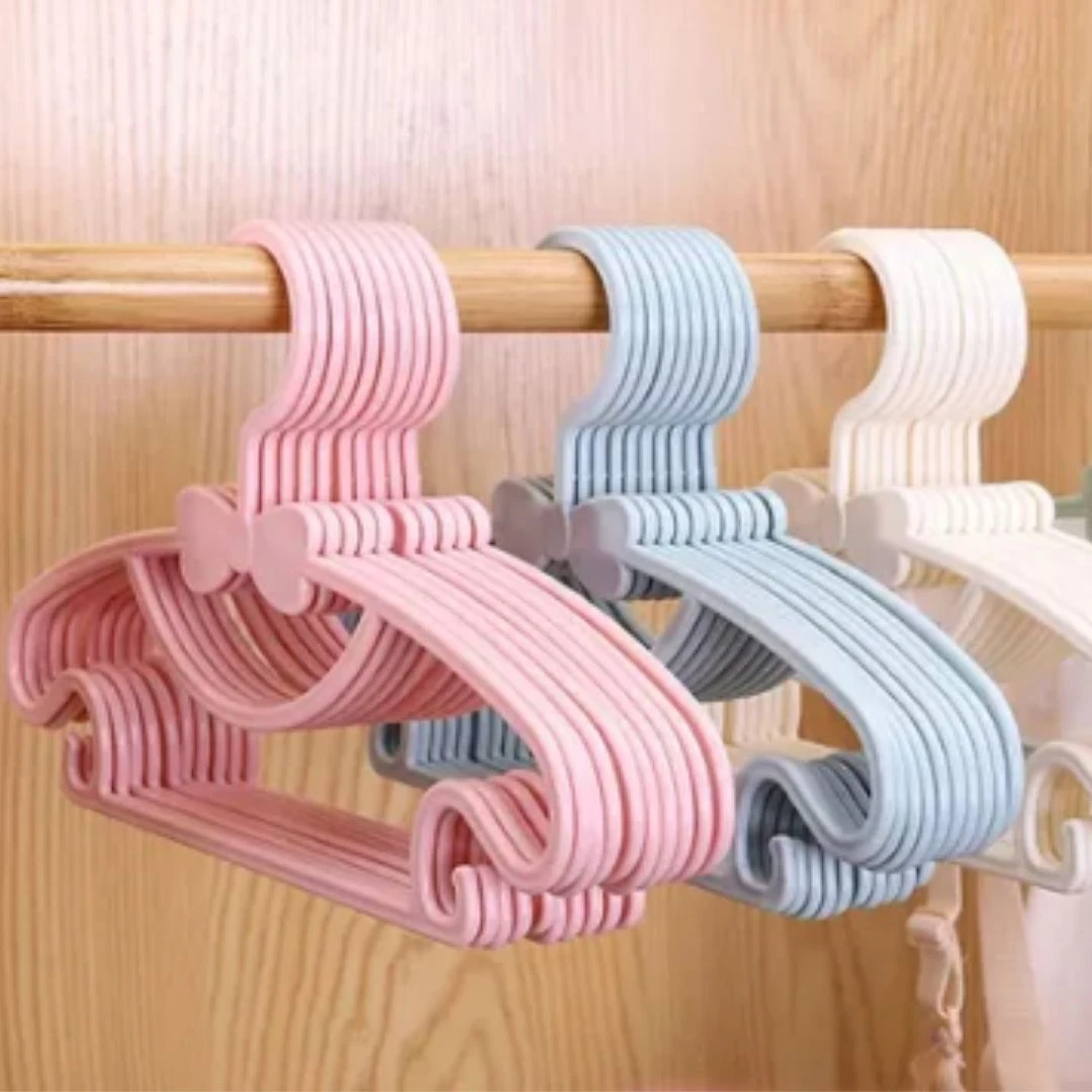 Ganchos flexibles rosados y celestes para ropa de bebé, con diseño antideslizante y forma de moño, organizando el clóset.