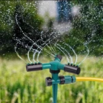 Aspersor de agua verde con 3 boquillas rociando en jardín.
