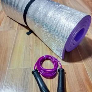 Colchoneta plateada enrollada con lazo morado, ideal para ejercicios en casa o al aire libre.