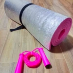 Colchoneta plateada enrollada con lazo rosado en el suelo de madera.