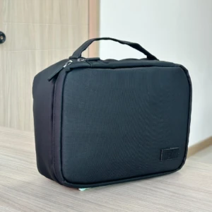 Cosmetiquera negra de tela resistente con asa superior, ideal para mujer.