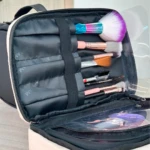 Cosmetiquera negra abierta mostrando compartimentos con brochas de maquillaje y accesorios dentro.