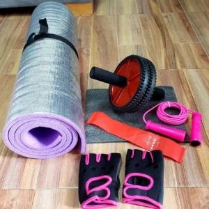 Kit de ejercicio con tapete morado enrollado, rueda abdominal roja, banda elástica naranja, cuerda de saltar rosa y guantes negros con detalles rosas.