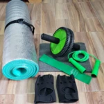 Kit de ejercicio con tapete enrollado, rueda abdominal verde, banda elástica y cuerda de saltar.