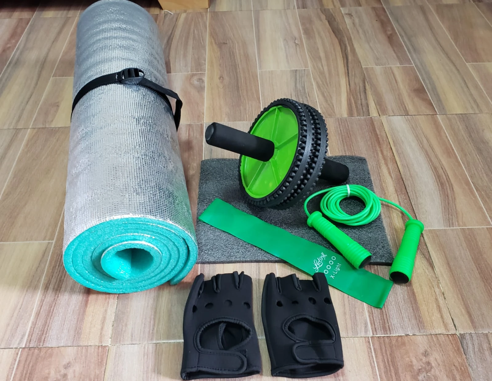 Kit de ejercicio con tapete enrollado, rueda abdominal verde, banda elástica y cuerda de saltar.