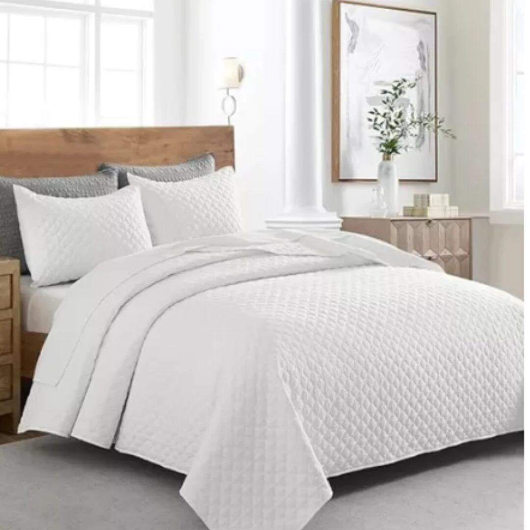 Colcha española blanca acolchada doble faz, vista de cerca en cama con almohadas a juego.