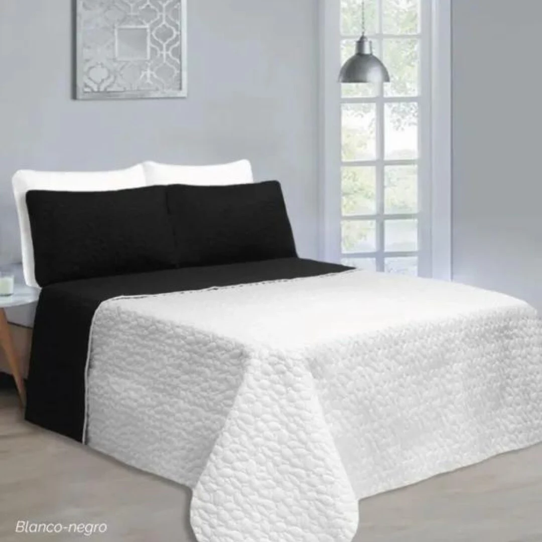 Colcha española doble faz blanco con patrón texturizado y almohadas negras, vista frontal.