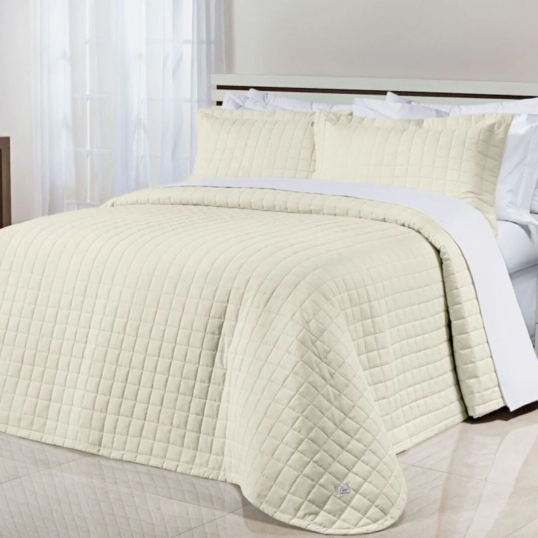 Colcha española doble faz, color marfil, textura acolchada, con cojines a juego sobre cama, para dormitorio.