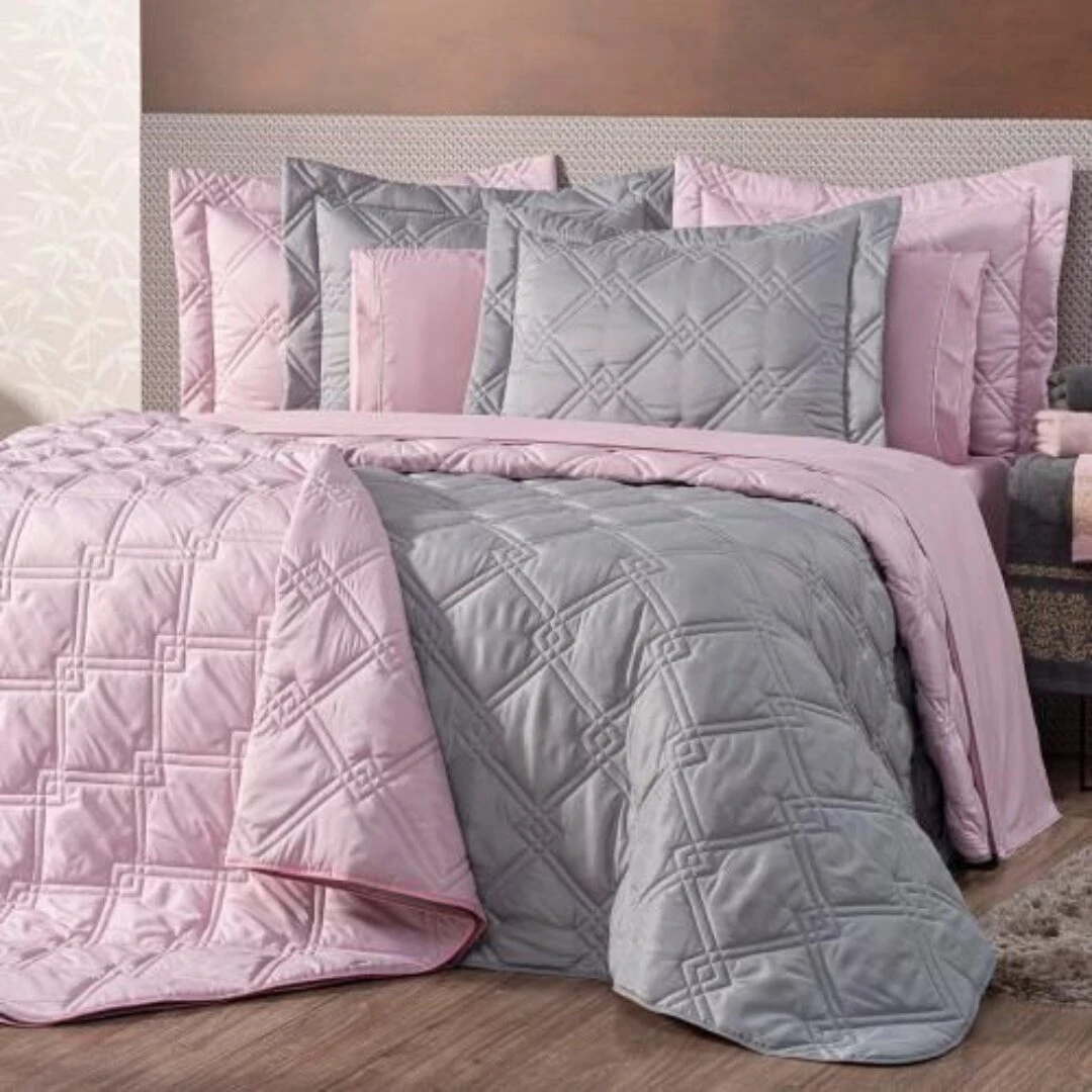 Colcha española doble faz rosa y gris con relieve geométrico, presentada en cama.