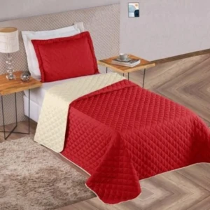 Colcha española doble faz roja y beige, acolchada, con almohada a juego, sobre cama con mesa auxiliar y alfombra.