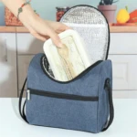 Lonchera térmica azul con interior plateado, mano guardando recipiente para almuerzo.